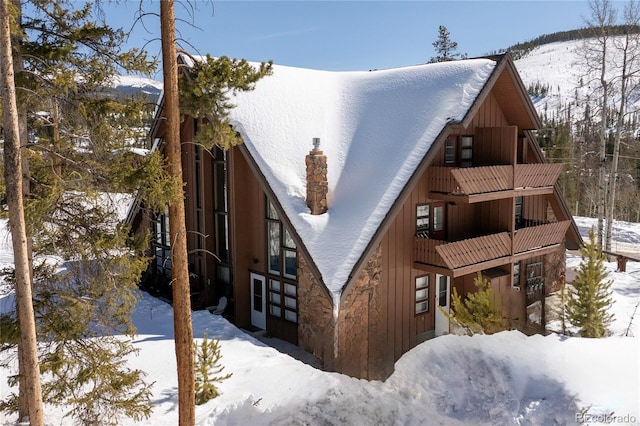 view of snow covered exterior with board and batten siding and a chimney