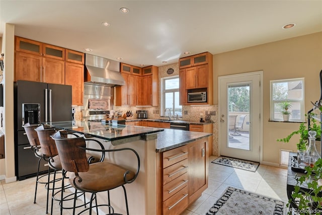 kitchen featuring a center island, wall chimney exhaust hood, black appliances, sink, and a kitchen breakfast bar