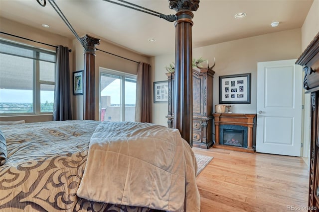 bedroom featuring a premium fireplace, access to exterior, light wood-type flooring, and decorative columns