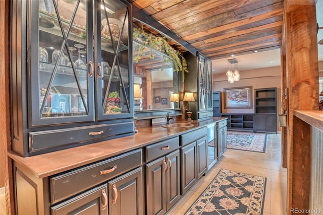 bar with sink, a chandelier, wooden ceiling, light tile patterned floors, and dark brown cabinets