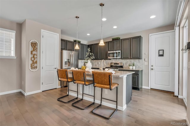 540 E Fremont Pl, Centennial, CO 80122 - kitchen with appliances with stainless steel finishes, light wood-style flooring, backsplash, a kitchen bar, and a center island with sink