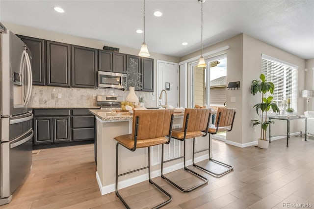 540 E Fremont Pl, Centennial, CO 80122 - kitchen featuring appliances with stainless steel finishes, tasteful backsplash, light wood-style floors, light stone countertops, and a breakfast bar area