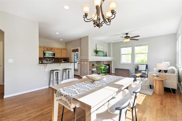 14247 W 84th Cir Unit A, Arvada, CO 80005 - dining space with a fireplace, light wood-style floors, a ceiling fan, a chandelier, and recessed lighting