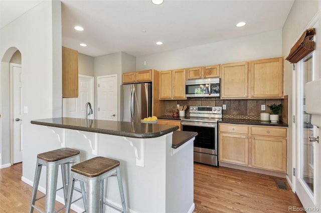 14247 W 84th Cir Unit A, Arvada, CO 80005 - kitchen featuring appliances with stainless steel finishes, light brown cabinets, dark countertops, a kitchen breakfast bar, and recessed lighting