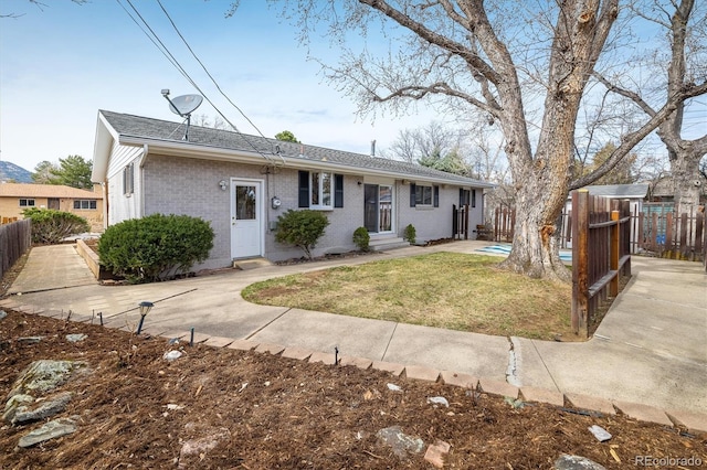 single story home featuring entry steps, brick siding, a front lawn, and fence