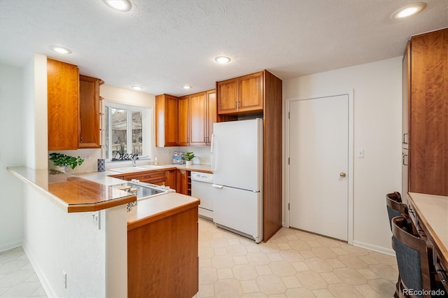 kitchen with white appliances, brown cabinetry, a peninsula, a sink, and light countertops