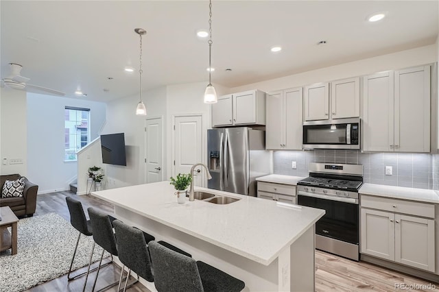 kitchen with appliances with stainless steel finishes, a sink, light wood-style flooring, tasteful backsplash, and open floor plan