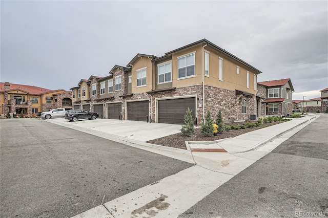 view of side of home with an attached garage, driveway, stucco siding, stone siding, and a residential view