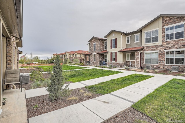 view of front facade with a front yard, stucco siding, cooling unit, stone siding, and a residential view