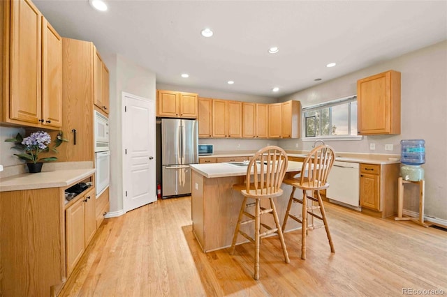10170 E 151st Ct, Brighton, CO 80602 - kitchen with white appliances, a breakfast bar area, a center island, light wood finished floors, and light brown cabinets