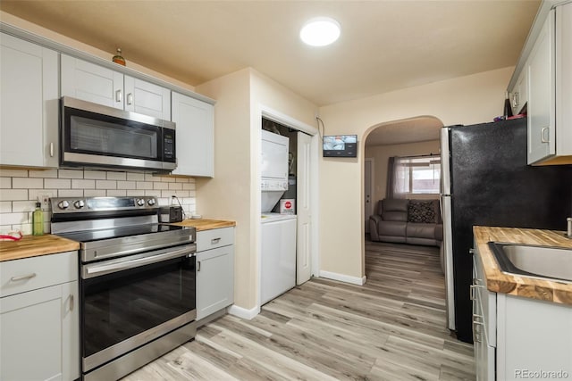 kitchen with light wood finished floors, decorative backsplash, stacked washer and clothes dryer, wood counters, and stainless steel appliances