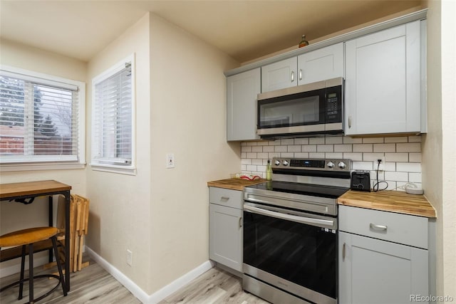 kitchen with appliances with stainless steel finishes, wooden counters, light wood-style flooring, and tasteful backsplash