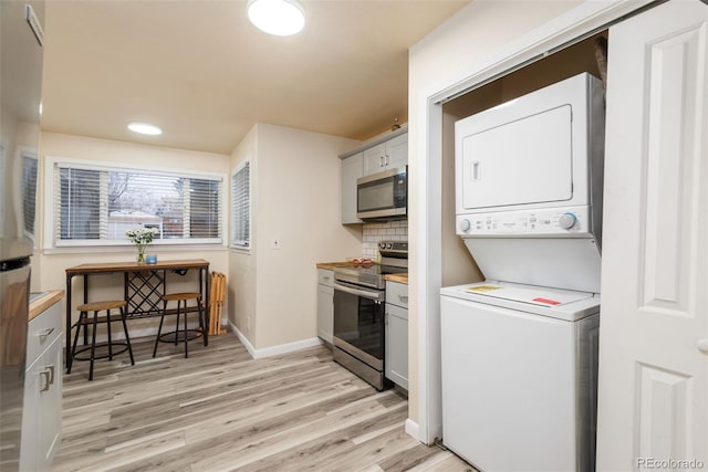 kitchen featuring stacked washer and dryer, baseboards, stainless steel appliances, light wood-type flooring, and backsplash