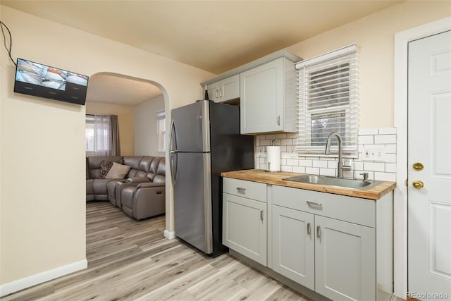 kitchen featuring arched walkways, wooden counters, backsplash, freestanding refrigerator, and a sink