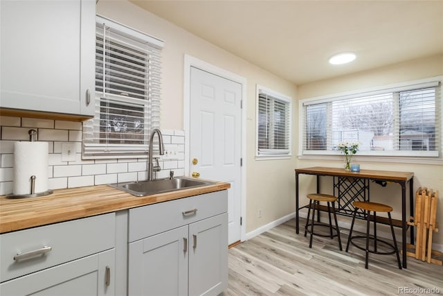 kitchen with butcher block counters, a sink, baseboards, light wood-style floors, and backsplash