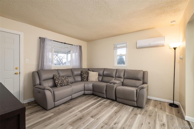 living area with light wood-style floors, a wealth of natural light, a wall unit AC, and a textured ceiling