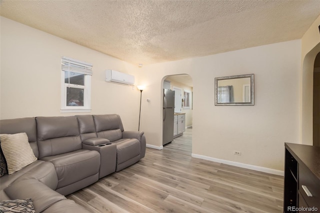 living room featuring baseboards, arched walkways, a wall unit AC, light wood-style flooring, and a textured ceiling