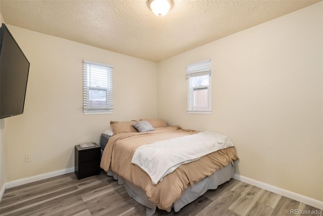 bedroom featuring a textured ceiling, light wood finished floors, and baseboards