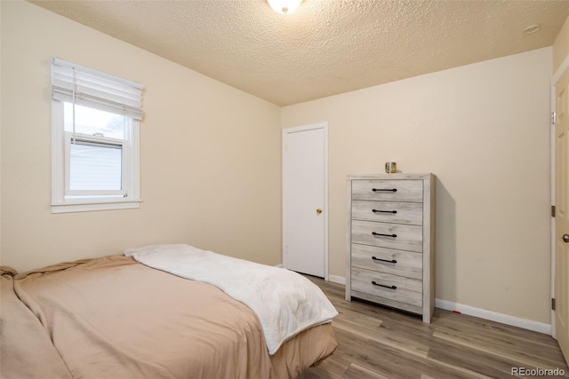 bedroom featuring a textured ceiling, baseboards, and wood finished floors