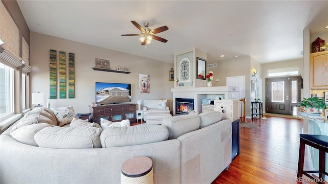 living area with a ceiling fan, visible vents, wood finished floors, and a glass covered fireplace