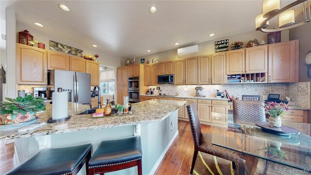 kitchen featuring light wood-style flooring, light stone counters, a breakfast bar, stainless steel appliances, and light brown cabinets