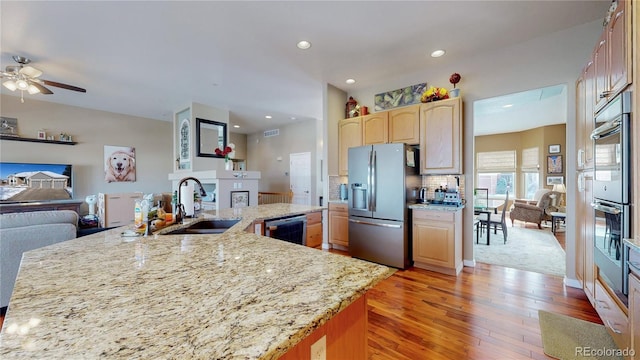 kitchen with light brown cabinets, stainless steel appliances, a fireplace, a sink, and open floor plan