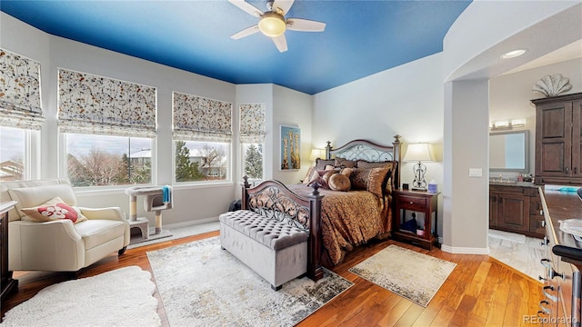 bedroom with baseboards, ceiling fan, light wood finished floors, and ensuite bathroom