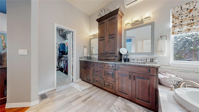 bathroom featuring a bathtub, double vanity, visible vents, a sink, and wood finished floors