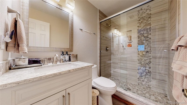 bathroom with toilet, a stall shower, a textured wall, and vanity