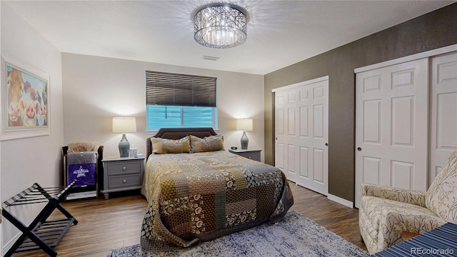 bedroom featuring two closets, visible vents, a chandelier, and dark wood-type flooring