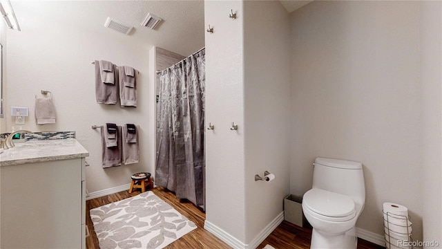 bathroom featuring baseboards, visible vents, toilet, wood finished floors, and vanity