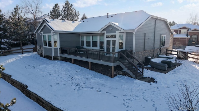 snow covered back of property with stone siding, fence, stairway, and a wooden deck