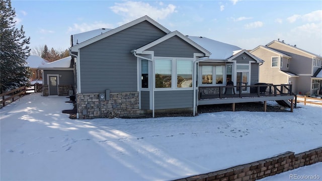 snow covered rear of property with stone siding and a wooden deck