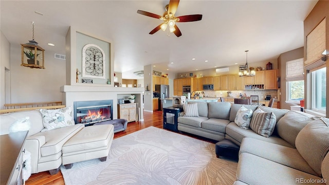 living room featuring visible vents, a ceiling fan, a glass covered fireplace, light wood-style flooring, and recessed lighting