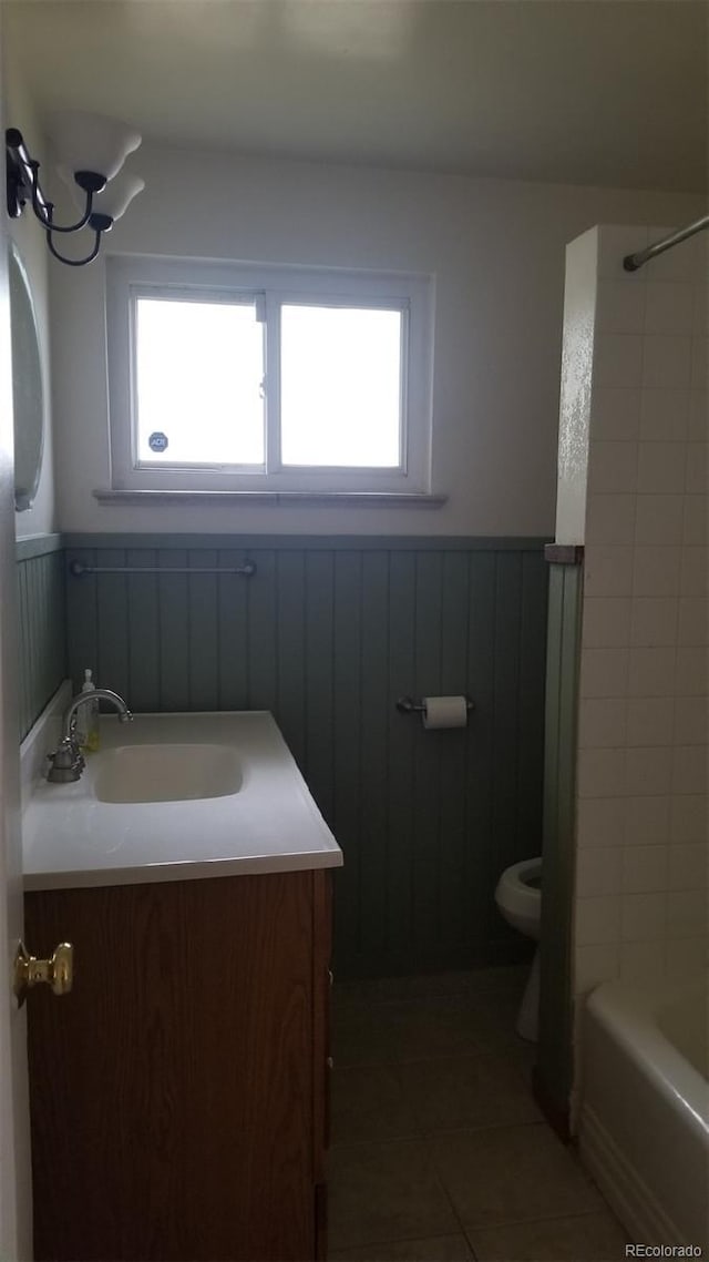 full bathroom with tile patterned floors, toilet, a healthy amount of sunlight, and wainscoting