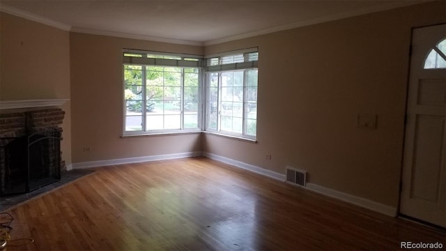 unfurnished living room with visible vents, a brick fireplace, wood finished floors, and crown molding