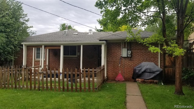 rear view of property with fence, brick siding, roof with shingles, and a lawn