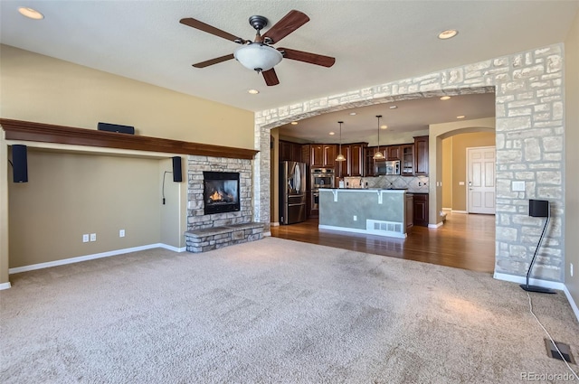 unfurnished living room featuring ceiling fan, a fireplace, and dark colored carpet