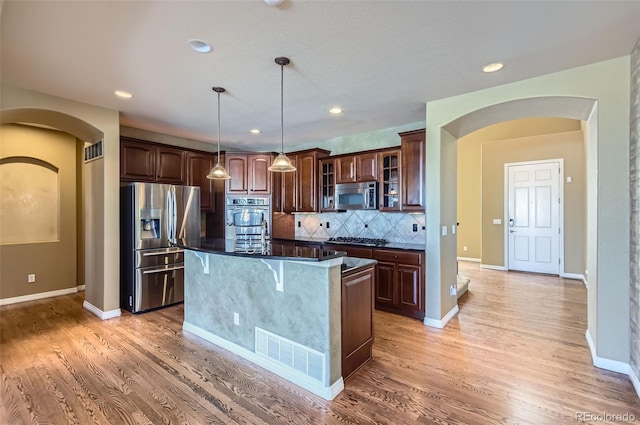 kitchen featuring tasteful backsplash, appliances with stainless steel finishes, pendant lighting, a kitchen island, and light wood-type flooring