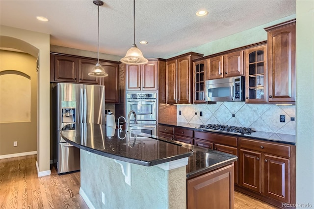 kitchen with a kitchen island with sink, light hardwood / wood-style flooring, a textured ceiling, appliances with stainless steel finishes, and decorative light fixtures