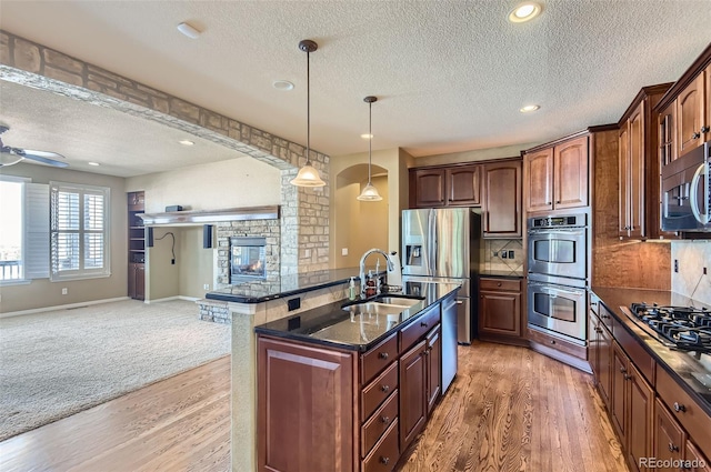 kitchen featuring sink, a fireplace, decorative light fixtures, wood-type flooring, and stainless steel appliances