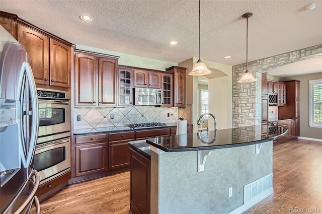 kitchen with hanging light fixtures, light hardwood / wood-style floors, a textured ceiling, and appliances with stainless steel finishes