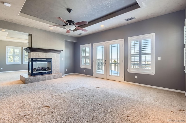 unfurnished living room featuring a tile fireplace, carpet floors, and a tray ceiling