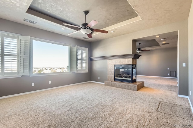 unfurnished living room with carpet, a tray ceiling, ceiling fan, and a tiled fireplace