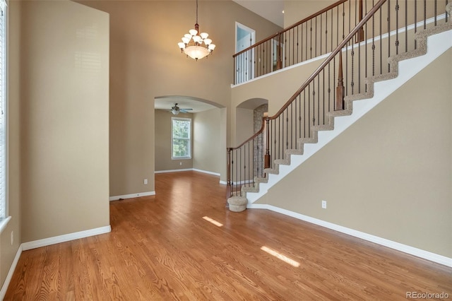 entryway with a towering ceiling, arched walkways, wood finished floors, stairway, and baseboards