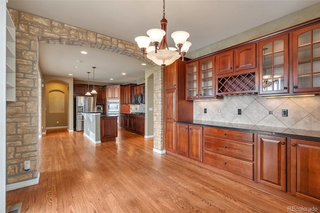 kitchen with dark countertops, appliances with stainless steel finishes, arched walkways, a chandelier, and light wood-style flooring