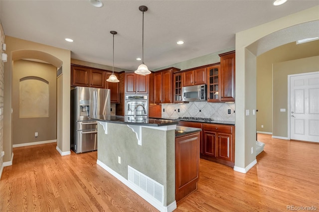 kitchen featuring dark countertops, appliances with stainless steel finishes, light wood-style floors, and arched walkways
