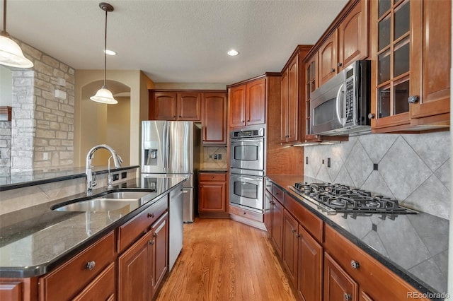 kitchen featuring a sink, dark stone countertops, stainless steel appliances, tasteful backsplash, and glass insert cabinets