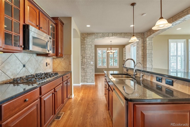 kitchen with ornate columns, light wood-type flooring, arched walkways, a sink, and appliances with stainless steel finishes