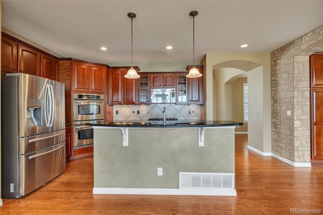 kitchen featuring dark countertops, a kitchen breakfast bar, arched walkways, light wood finished floors, and appliances with stainless steel finishes